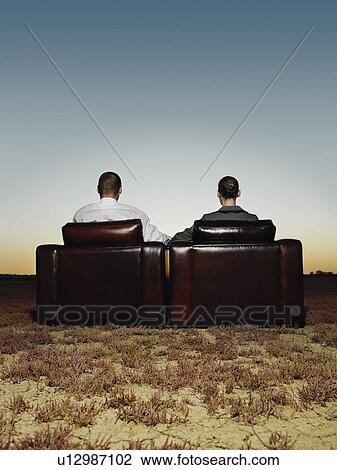 Stock Image - Two business people in armchairs in open plain at sunset back view. Fotosearch