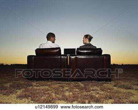 Stock Photo - Two business people in armchairs in open plain at sunset. Fotosearch