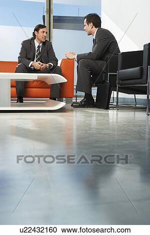 Stock Image - Two businessmen having meeting in lobby. Fotosearch