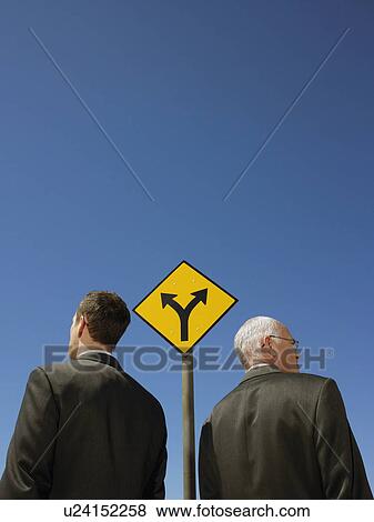 Stock Photo - Two businessmen standing by road sign half length back view. Fotosearch