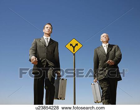 Two businessmen walking past road sign View Large Photo Image Stock Photo - Two businessmen walking past road sign. Fotosearch