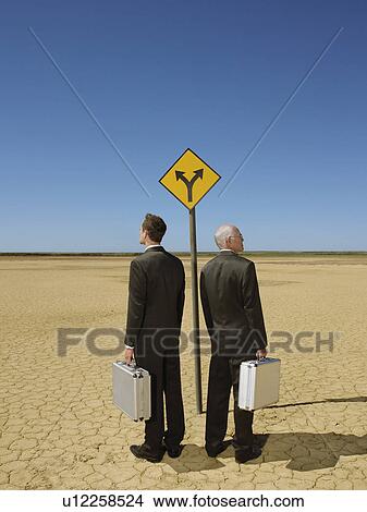 Two businessmen with briefcases standing by road sign in desert full length back view View Large Photo Image Picture - Two businessmen with briefcases standing by road sign in desert full length back view. Fotosearch