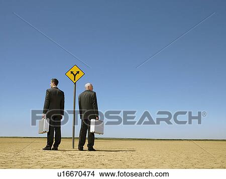 Two businessmen with briefcases standing by road sign in desert full length back view View Large Photo Image Picture - Two businessmen with briefcases standing by road sign in desert full length back view. Fotosearch