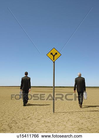 Two businessmen with briefcases walking past road sign in desert back view View Large Photo Image Stock Photograph - Two businessmen with briefcases walking past road sign in desert back view. Fotosearch