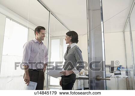 Stock Photo - Two businesspeople standing in office talking.. Fotosearch