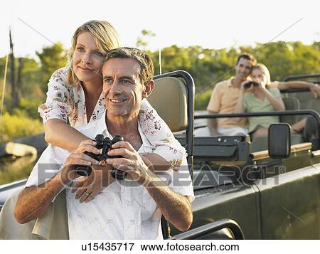Stock Photo - Two couples on trip one sitting in jeep using binoculars. Fotosearch