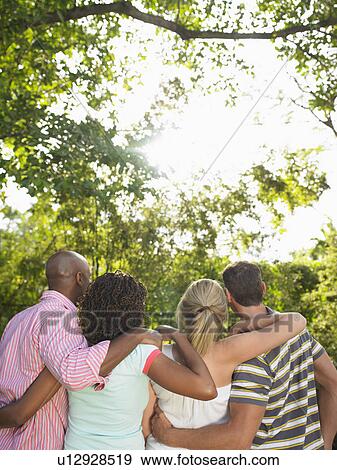 Stock Photo - Two couples standing arm in arm in garden back view. Fotosearch