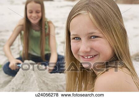 Two girls (10-12) playing in sand on beach focus on girl on foreground View Large Photo Image Stock Photo - Two girls (10-12) playing in sand on beach focus on girl on foreground. Fotosearch