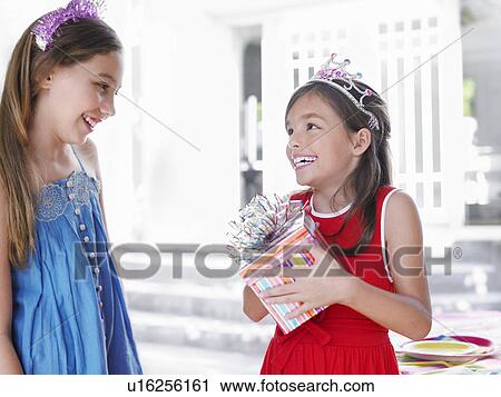 Stock Image - Two girls (7-9 10-12) at birthday party one holding present smiling. Fotosearch
