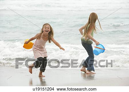 Two girls (7-9 10-12) holding buckets playing on beach View Large Photo Image Picture - Two girls (7-9 10-12) holding buckets playing on beach. Fotosearch