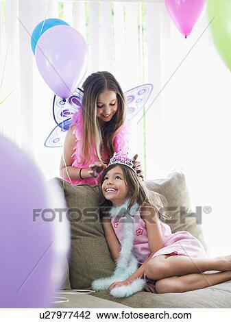 Two girls (7-9 10-12) on sofa in party costumes one adjusting other's tiara View Large Photo Image Stock Image - Two girls (7-9 10-12) on sofa in party costumes one adjusting other's tiara. Fotosearch