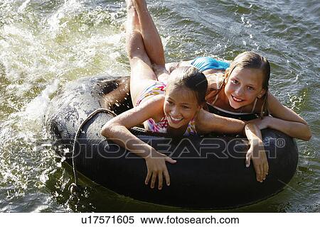 Stock Photography - Two girls (7-9) lying on float tube elevated view.. Fotosearch