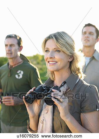 Stock Photography - Two men and woman looking at view woman holding binoculars. Fotosearch