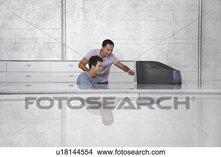 Picture - Two men in front of television set one pointing at screen. Fotosearch