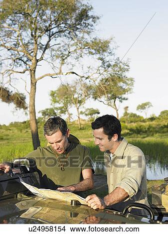 Picture - Two men reading map spread on bonnet of jeep. Fotosearch