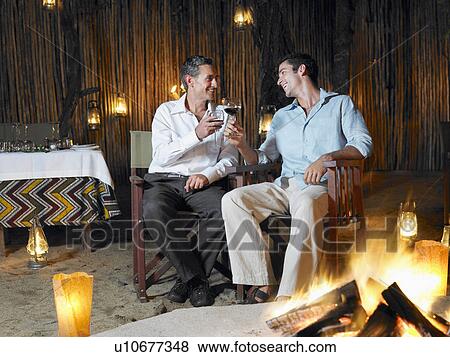 Two men sitting by bonfire at outdoor nightclub toasting View Large Photo Image Stock Photo - Two men sitting by bonfire at outdoor nightclub toasting. Fotosearch