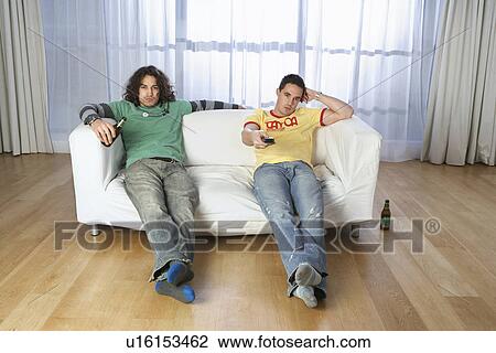Stock Image - Two men sitting on sofa watching television. Fotosearch