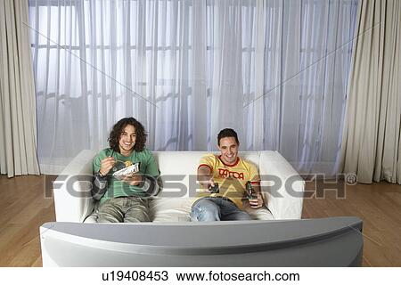 Stock Image - Two men sitting on sofa watching television. Fotosearch