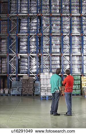Stock Photo - Two Men standing side by side Looking at Full Warehouse Shelves back view. Fotosearch