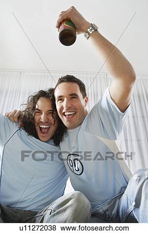Two men watching television and cheering with beer bottle View Large Photo Image Stock Photo - Two men watching television and cheering with beer bottle. Fotosearch