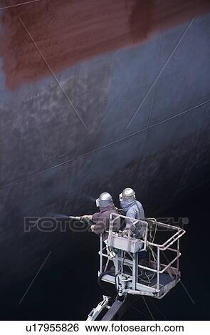Stock Photograph - Two People standing in crane bucket Painting Large Ship. Fotosearch
