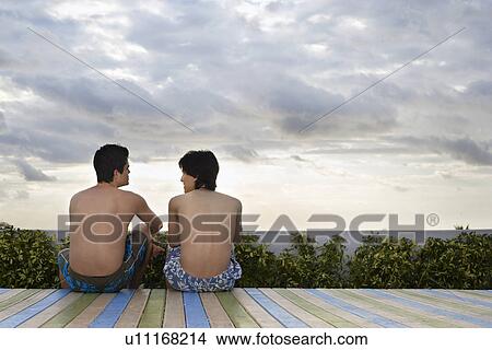 Two teenage boys (16-17) sitting on wooden deck back view View Large Photo Image Picture - Two teenage boys (16-17) sitting on wooden deck back view. Fotosearch