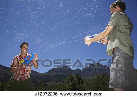 Stock Photograph - Two teenage boys (16-17 years) fighting with squirt guns in mountains. Fotosearch