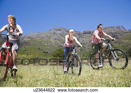 Stock Image - Two teenage boys and girl (16-17 years) biking mountains in background. Fotosearch