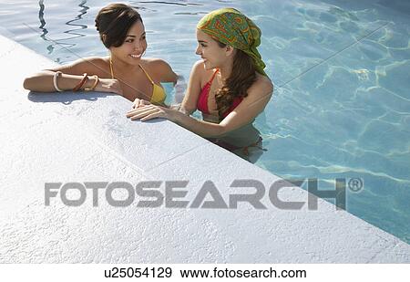 Stock Photo - Two teenage girls (16-17) standing in swimming pool elevated view. Fotosearch