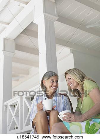 Two women holding coffee mugs sitting on verandah low angle view View Large Photo Image Stock Photography - Two women holding coffee mugs sitting on verandah low angle view. Fotosearch