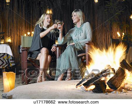 Two women sitting by bonfire at outdoor nightclub toasting View Large Photo Image Stock Image - Two women sitting by bonfire at outdoor nightclub toasting. Fotosearch