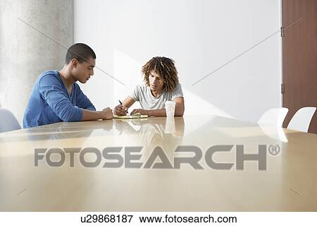 Stock Photo - Two young men sitting at conference table. Fotosearch