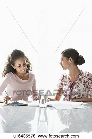 Stock Photo - Two young women sitting at table writing on paper. Fotosearch