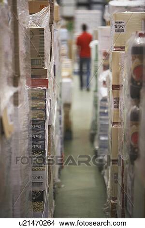 Picture - Warehouse Full of cellophane-wrapped Goods warehouse worker in background back view. Fotosearch
