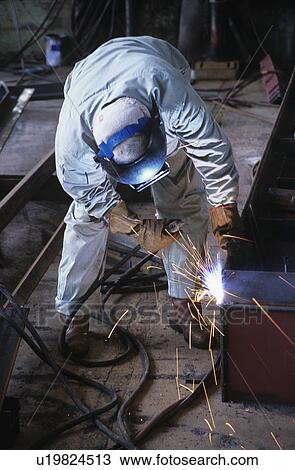 Stock Image - Welder bending down welding at Work. Fotosearch
