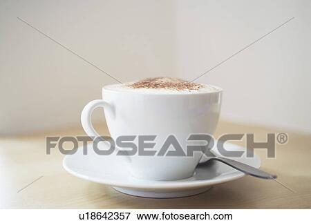 Stock Photo - White cup of cappuccino on wooden table close-up. Fotosearch