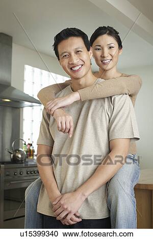 Stock Image - Wife sitting on countertop arms around standing husband. Fotosearch