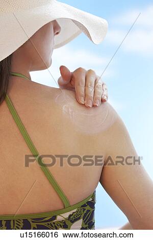 Stock Photograph - Woman applying sunscreen to shoulder back view. Fotosearch