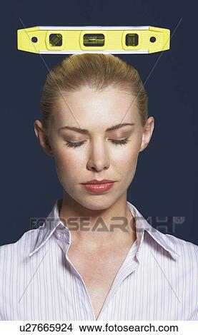 Picture - Woman balancing spirit level on her head against dark background. Fotosearch