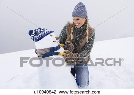 Woman dressing snowman kneeling on snow-covered hill View Large Photo Image Stock Image - Woman dressing snowman kneeling on snow-covered hill. Fotosearch