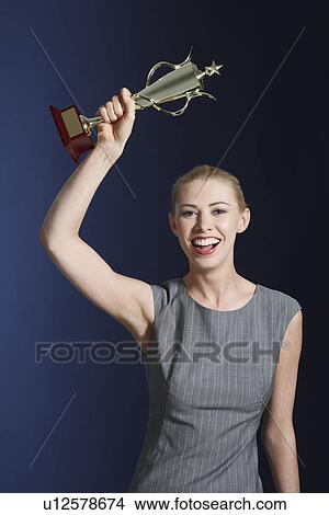 Picture - Woman hoisting trophy over head against dark background. Fotosearch