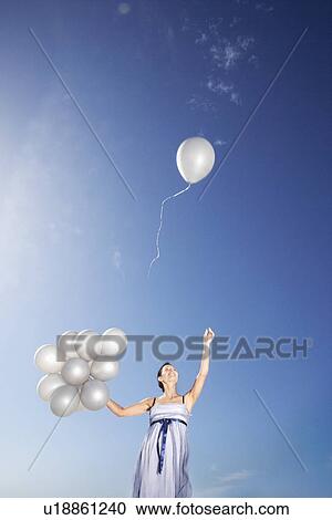 Woman holding balloons against sky one flying away low angle view View Large Photo Image Stock Image - Woman holding balloons against sky one flying away low angle view. Fotosearch