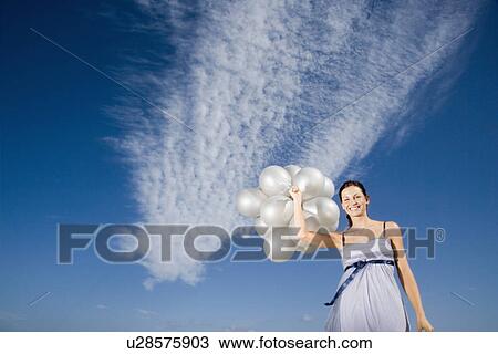 Stock Image - Woman holding balloons against sky portrait low angle view. Fotosearch
