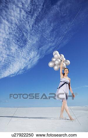Stock Image - Woman holding balloons on beach. Fotosearch