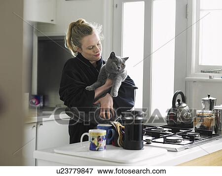 Stock Photo - Woman holding cat standing in kitchen. Fotosearch