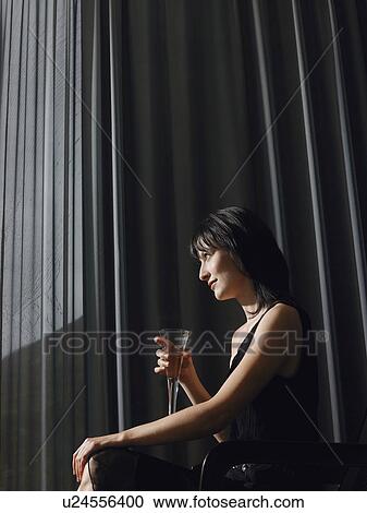Woman holding champagne in front of curtains indoors side view View Large Photo Image Stock Image - Woman holding champagne in front of curtains indoors side view. Fotosearch