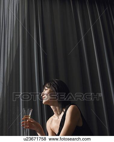 Woman holding champagne in front of curtains indoors View Large Photo Image Stock Photo - Woman holding champagne in front of curtains indoors. Fotosearch