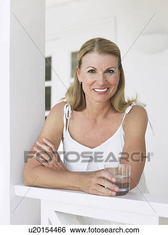 Woman holding glass of water leaning on verandah balustrade portrait View Large Photo Image Stock Photograph - Woman holding glass of water leaning on verandah balustrade portrait. Fotosearch