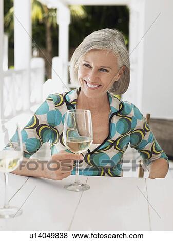 Stock Photo - Woman holding glass of wine at verandah table portrait. Fotosearch