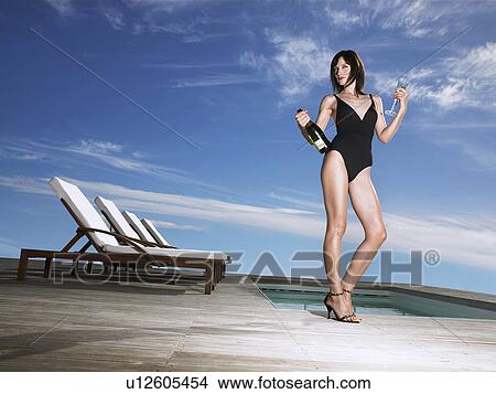 Picture - Woman in bathing suit holding champagne at poolside. Fotosearch